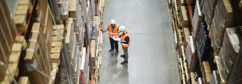 Por que utilizar o Cross Docking? Na imagem, vemos trabalhadores verificando mercadorias para transporte, cujo processo pode ser otimizado por meio do sistema cross docking