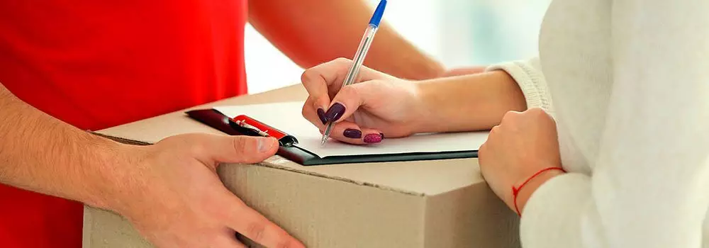 Como funciona o Just in Time? Na imagem, mulher assinando documento após entrega de mercadoria, que tem a etapa do ponto pedido como essencial para início do processo